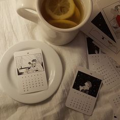 a cup of tea with lemon slices and calendars on the table next to it