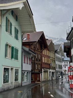 a wet street with buildings on both sides and mountains in the background