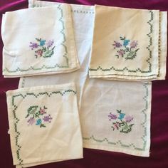 four embroidered napkins with flowers on them sitting on a purple cloth covered tablecloth