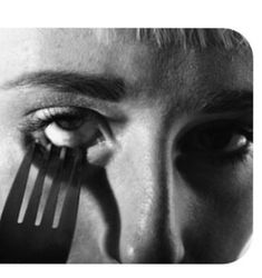 a close up of a person holding a fork in front of their eye and looking at the camera