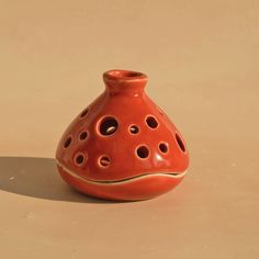 an orange ceramic vase with holes in the middle on a beige surface, sitting upright