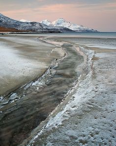 the beach is covered in ice and water with mountains in the background at sunset or dawn