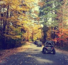 two atvs driving down a road in the woods with fall foliage on the trees