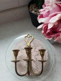 two brass candelabras on a glass plate with pink flowers in the background