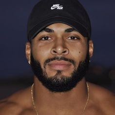 a man with a beard wearing a nike hat and gold chain around his neck is looking at the camera