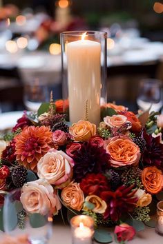 an arrangement of flowers and candles on a table with lights in the background at a wedding reception