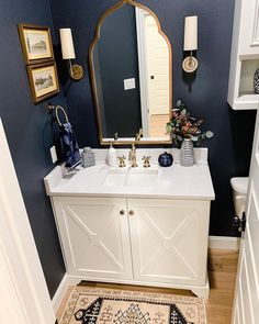 a bathroom with blue walls and white vanity, gold framed mirror, rugs on the floor