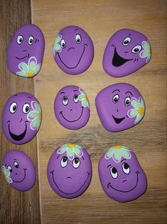 purple painted rocks with smiley faces and flowers on them, arranged in the shape of hearts