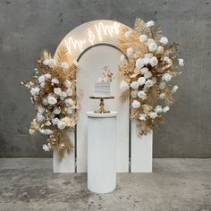 a wedding cake is displayed in front of an arch decorated with gold and white flowers