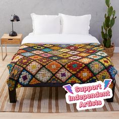 a bed with a colorful blanket on top of it next to a potted plant