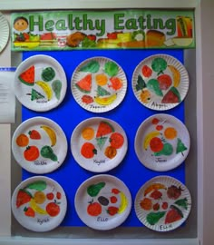 paper plates with different fruits and vegetables painted on them in front of a bulletin board