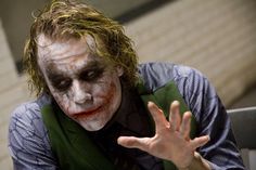 a man dressed as the joker holding his hand up in front of him with one hand out