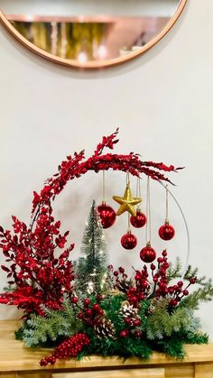 a christmas arrangement with red berries, greenery and baubles in front of a mirror