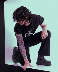 a man in black shirt kneeling down with his hand on the ground next to a skateboard