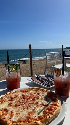 a pizza sitting on top of a white plate next to two glasses filled with drinks