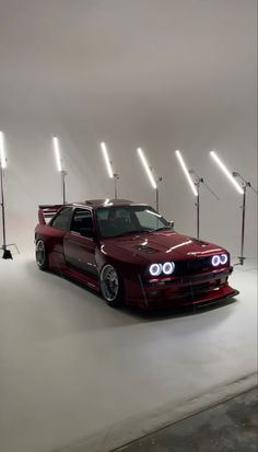 a red car parked in front of three lights on a white background with the hood down