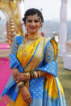 a woman in a yellow and blue sari is posing for the camera with her hands on her hips