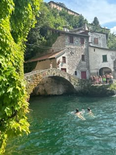 people are swimming in the water near an old stone building with a bridge over it