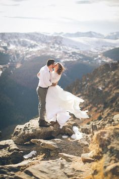 a bride and groom kissing on top of a mountain