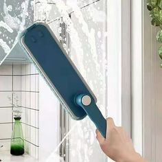 a person is holding a blue toothbrush in front of a window with water on it