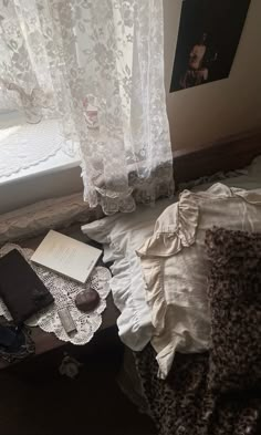 an unmade bed sitting next to a window with lace curtains on the windowsill