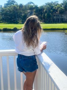 a woman standing on a bridge looking at the water and trees in the distance with her back to the camera