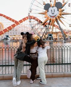 two girls hugging each other in front of a ferris wheel at an amusement park with mickey mouse