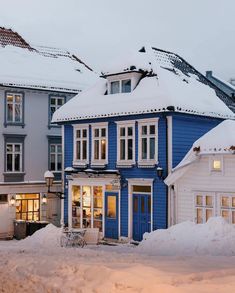 a blue house with snow on the roof and windows in front of it, surrounded by other houses