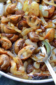 a skillet filled with onions and sausages on top of a table next to a spoon