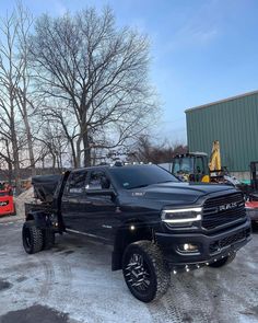 a large black truck parked in front of a building with other trucks behind it and snow on the ground