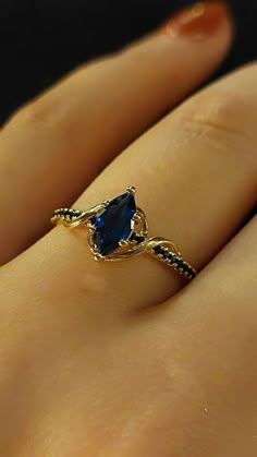 a woman's hand with a gold ring and blue stone in the middle, on top of her finger