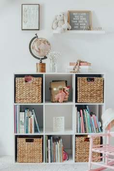 a white book shelf filled with lots of books next to a pink rocking chair and teddy bear