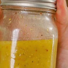 a hand holding a glass jar filled with yellow liquid and seasoning on the inside