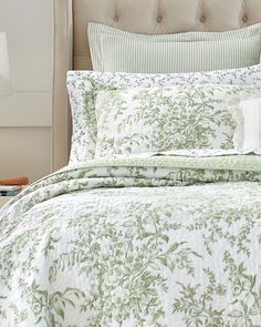 a bed with a green and white comforter on top of it next to a night stand