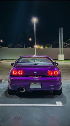 a purple sports car parked in a parking lot at night with its lights turned on