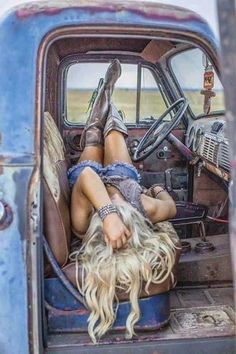 a woman laying on the back of an old blue truck with her legs spread out