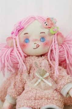 a doll with pink hair and blue eyes sitting on a white surface in front of a wall