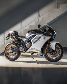 a white and black motorcycle parked in front of some stairs with the sun shining on it