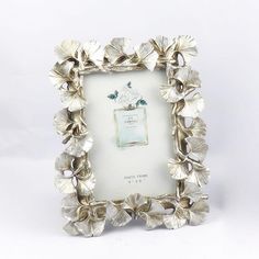 a silver frame with flowers and a bottle in the center on a white background,