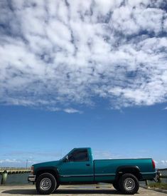 a blue pick up truck parked in front of a body of water under a partly cloudy sky