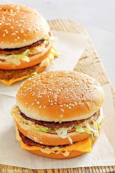 two hamburgers with cheese and lettuce sitting on top of white paper napkins