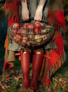 a woman in red boots holding a basket filled with apples