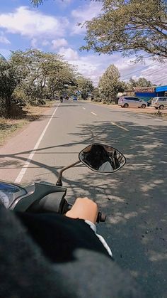 a person riding a motorcycle down a street next to a tree lined road with parked cars