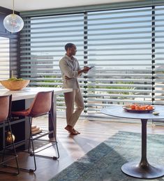 a man standing in front of a window next to a table with fruit on it