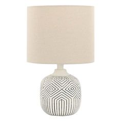 a table lamp with a white and black design on the base, next to a beige shade