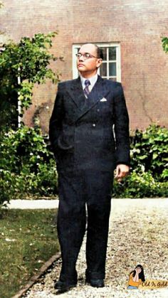 a man in a suit and tie standing on gravel next to a building with trees