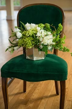 a green chair with flowers and greenery on it sitting in a wood floored room