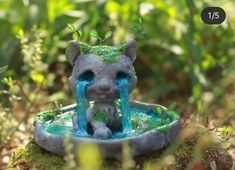 a statue of a cat drinking water out of a fountain in the middle of some grass