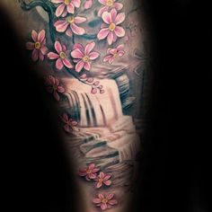 a woman's arm with pink flowers on it and a waterfall in the background