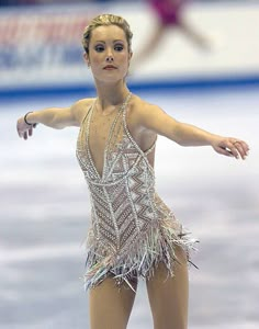 a woman skating on an ice rink wearing a feathery dress and holding her arms out